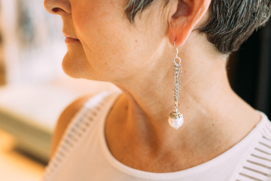 A woman wearing Carolily Finery earrings made from European pearl, sterling silver accents, stainless steel chains and earwires