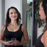 A woman smiling into the mirror wearing a Carolily Finery statement necklace made from sterling silver, onyx and European crystal pearls