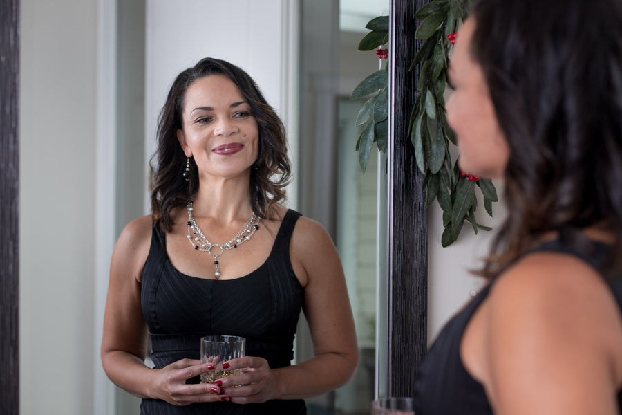 A woman smiling into the mirror wearing a Carolily Finery statement necklace made from sterling silver, onyx and European crystal pearls