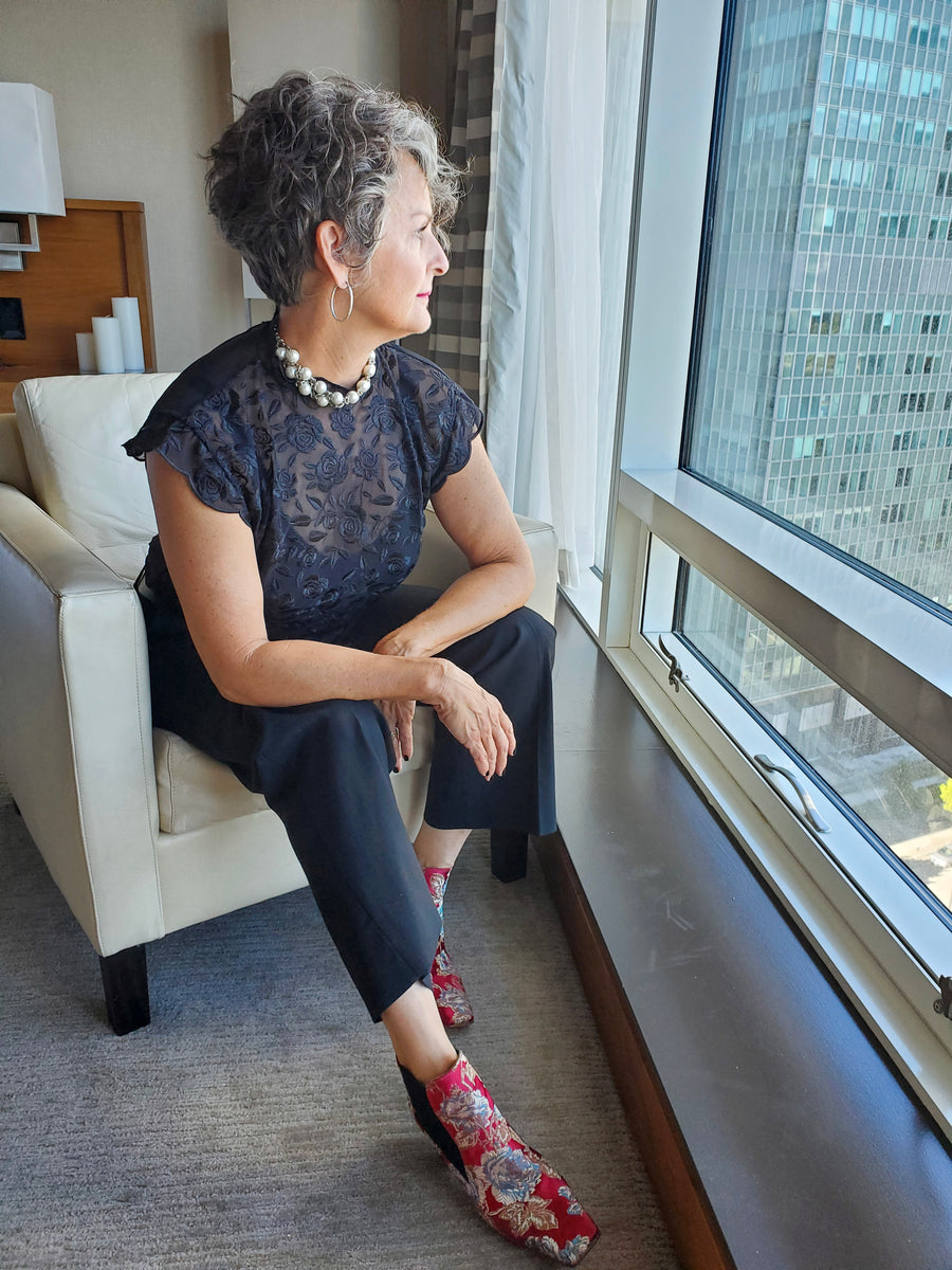 A woman sitting in a chair looking out the window wearing a Carolily Finery statement necklace made from stainless steel chain and large European white crystal pearls