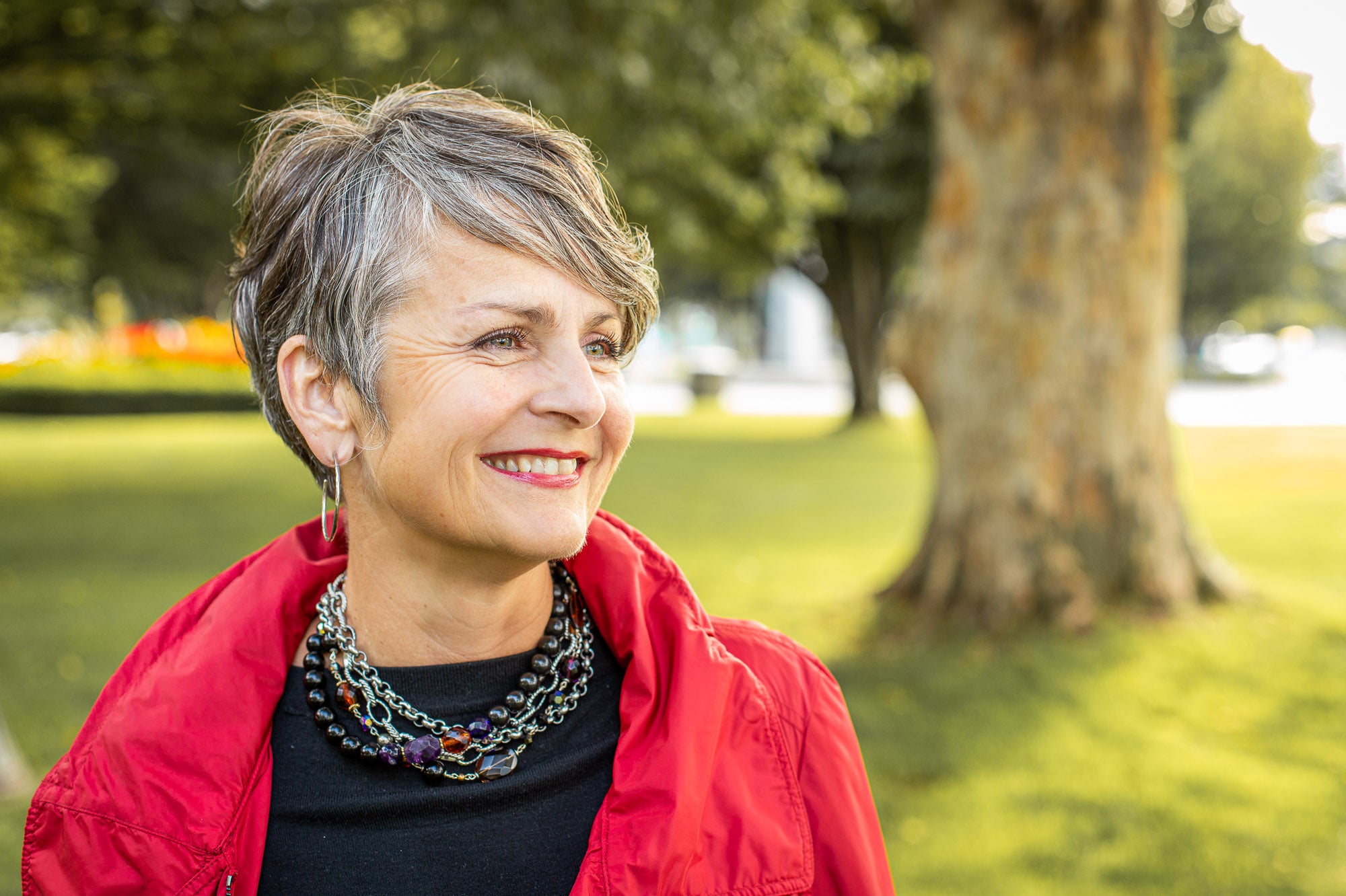 A woman in a red jacket wearing a Carolily Finery necklace made from silver chain, black onyx, various gemstones and Swarovski crystal