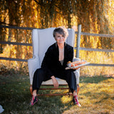 A woman in an armchair wearing a Carolily Finery statement necklace made from silver plated chain and European crystal pearls